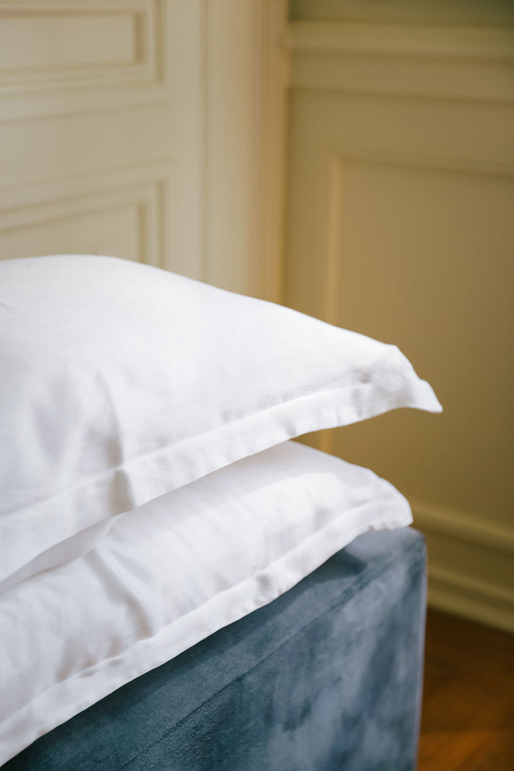 Two pillows with white pillowcases made with silk from orange peel on a blue teal velvet sofa.