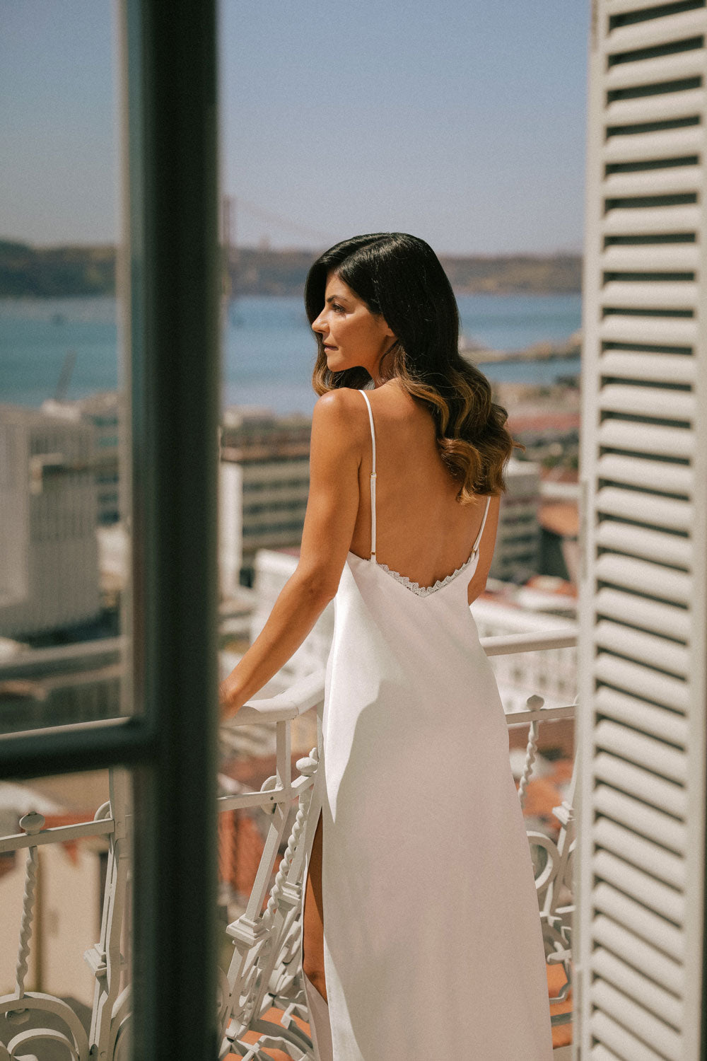 woman from the back, on a porch, dressed in a long white silk nightgown.