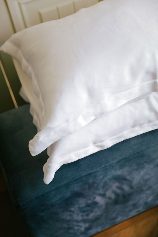 Two pillows with white pillowcases made with silk from orange peel on a blue teal velvet sofa, seen from the top.